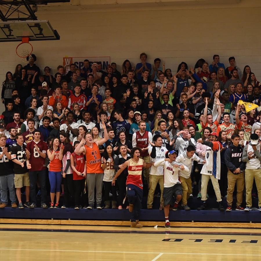 A bunch of jersey-wearing WS basketball fans gather together at a home game to cheer on their classmates.