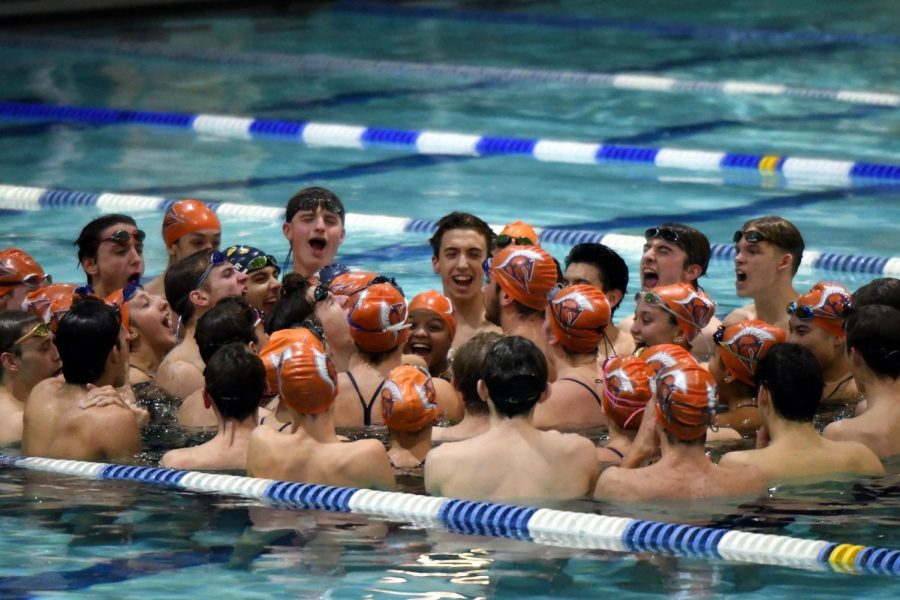The swim team gathers for their pre-meet cheer in whey they progressively yell louder and louder until they are screaming at the top of their lungs in order to get themselves fired up for their meet.