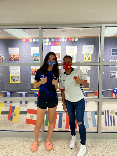 Two out of the three SEALs, Keira Walker and Jasmyn Rolison, stand in front of one of the Hispanic Heritage Month displays in the school that highlight accomplished members of the Latinx community.