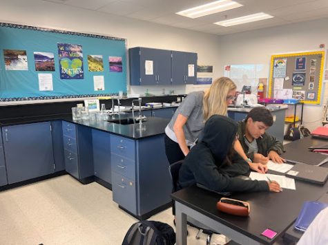 Teacher Heidi Averette helping her ninth grade biology students with questions where they apply their knowledge about graphing and experimental design with an exercising and heart rate experiment outside.