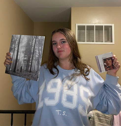Junior Sylvia McCauley poses with her collection of Taylor Swift merchandise including a 1989 sweatshirt, folklore vinyl record, and a Midnights CD.
