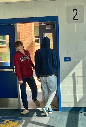 A student opens door two, allowing another student in during the class transition period.